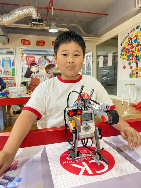 A student in a CK Education shirt with the walking robot he built from LEGO and a programmable controller